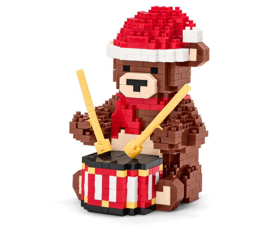 Ein brauner Bären-Bausatz mit roter Mütze und Schal spielt mit Trommelstöcken auf einer Trommel.