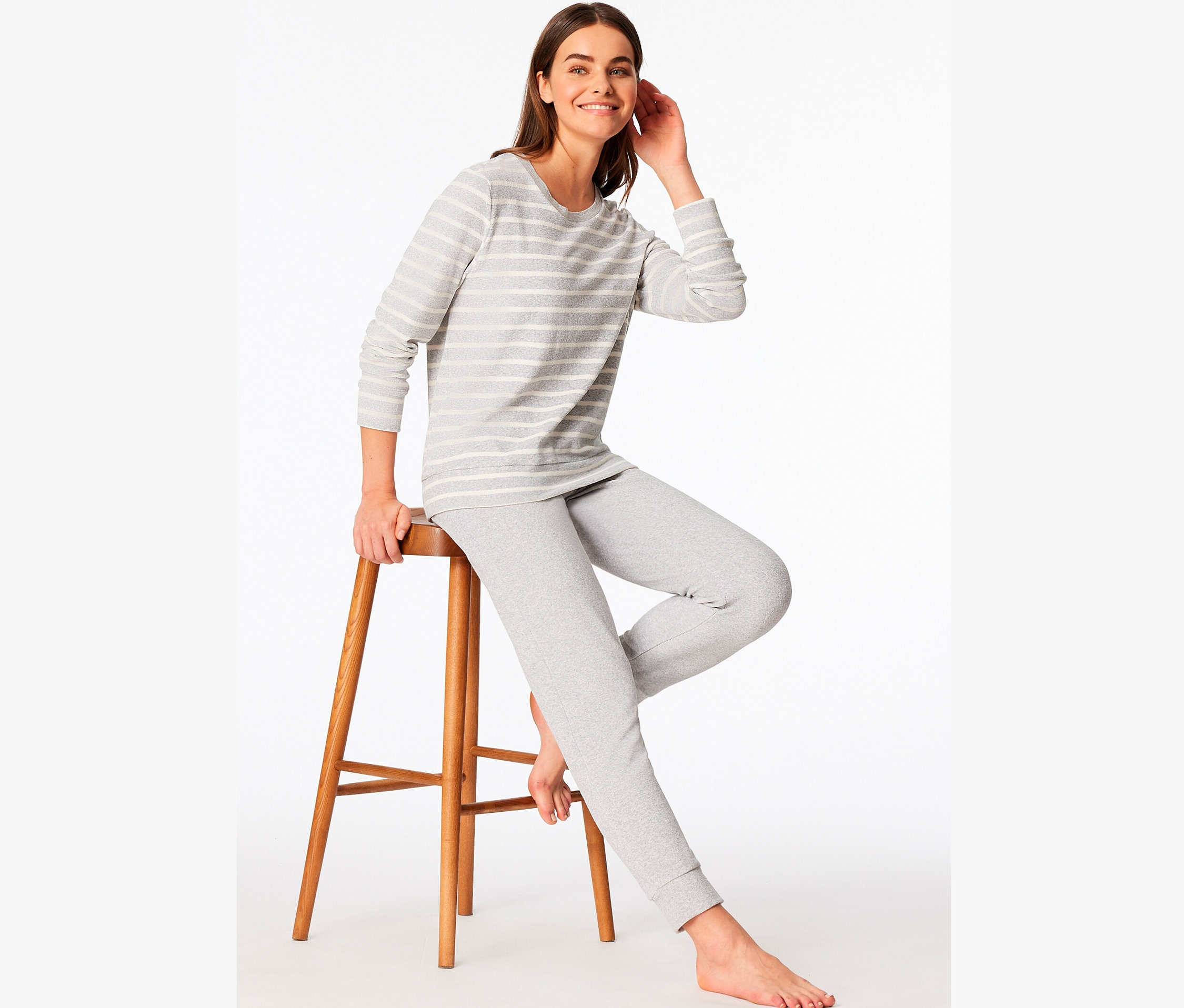 Frau sitzt auf einem Holzstuhl und trägt einen grau gestreiften Pyjama.