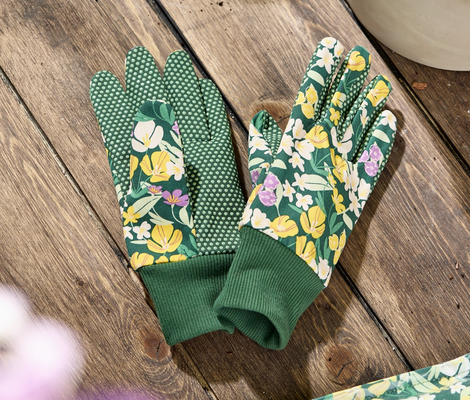 Auf einem Holztisch liegt ein Paar Garten-Handschuhe mit Blumenmuster.