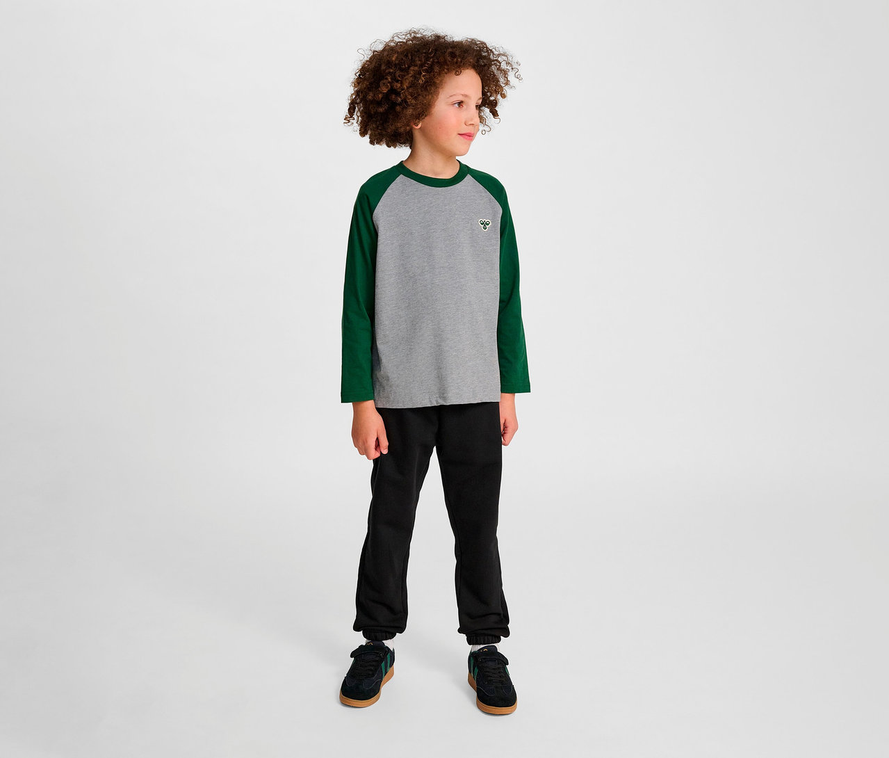 Junge steht und trägt ein grünes HUMMEL HMLJR Raglan Loose T-Shirt.