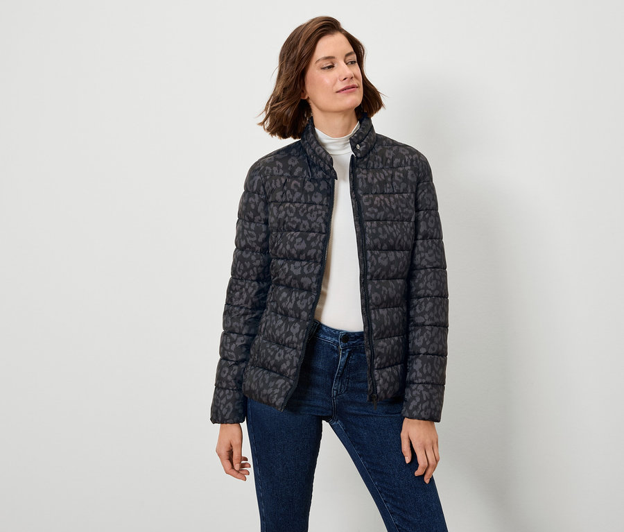 Frau trägt eine schwarze Daunenjacke mit Muster und Jeans.