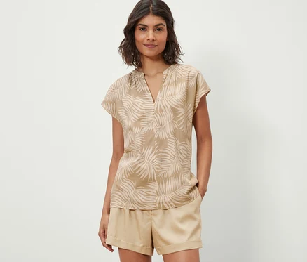 Frau trägt eine bedruckte Kurzarmbluse in Beige.