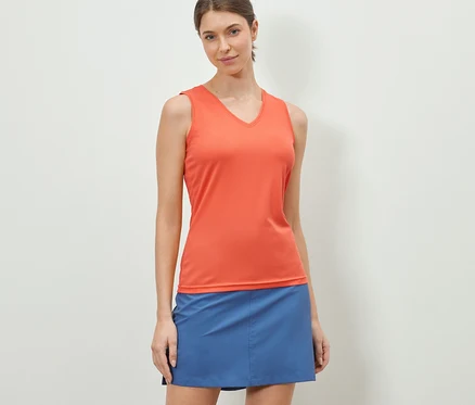 Eine Frau trägt ein orangefarbenes V-Neck-Funktionstop und einen blauen Rock.