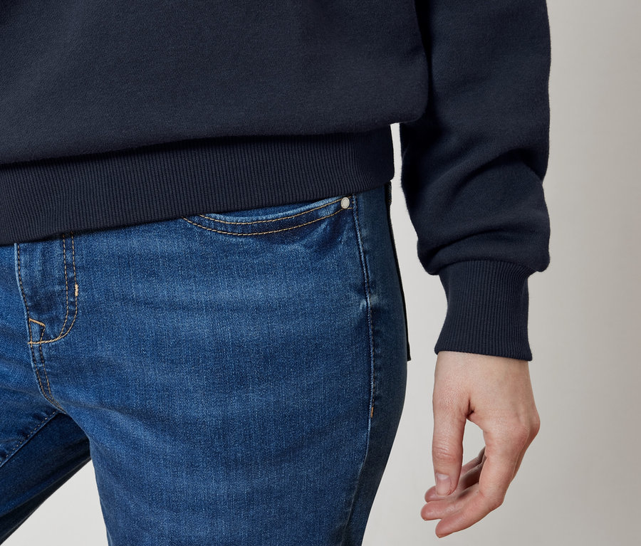 Detailaufnahme von blauen Jeans und einem dunkelblauen Pullover an einer Person.