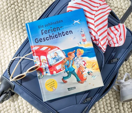 Auf einem blauen Koffer liegen das Buch »Die schönsten Feriengeschichten«, eine Sonnenbrille und ein gestreiftes T-Shirt.