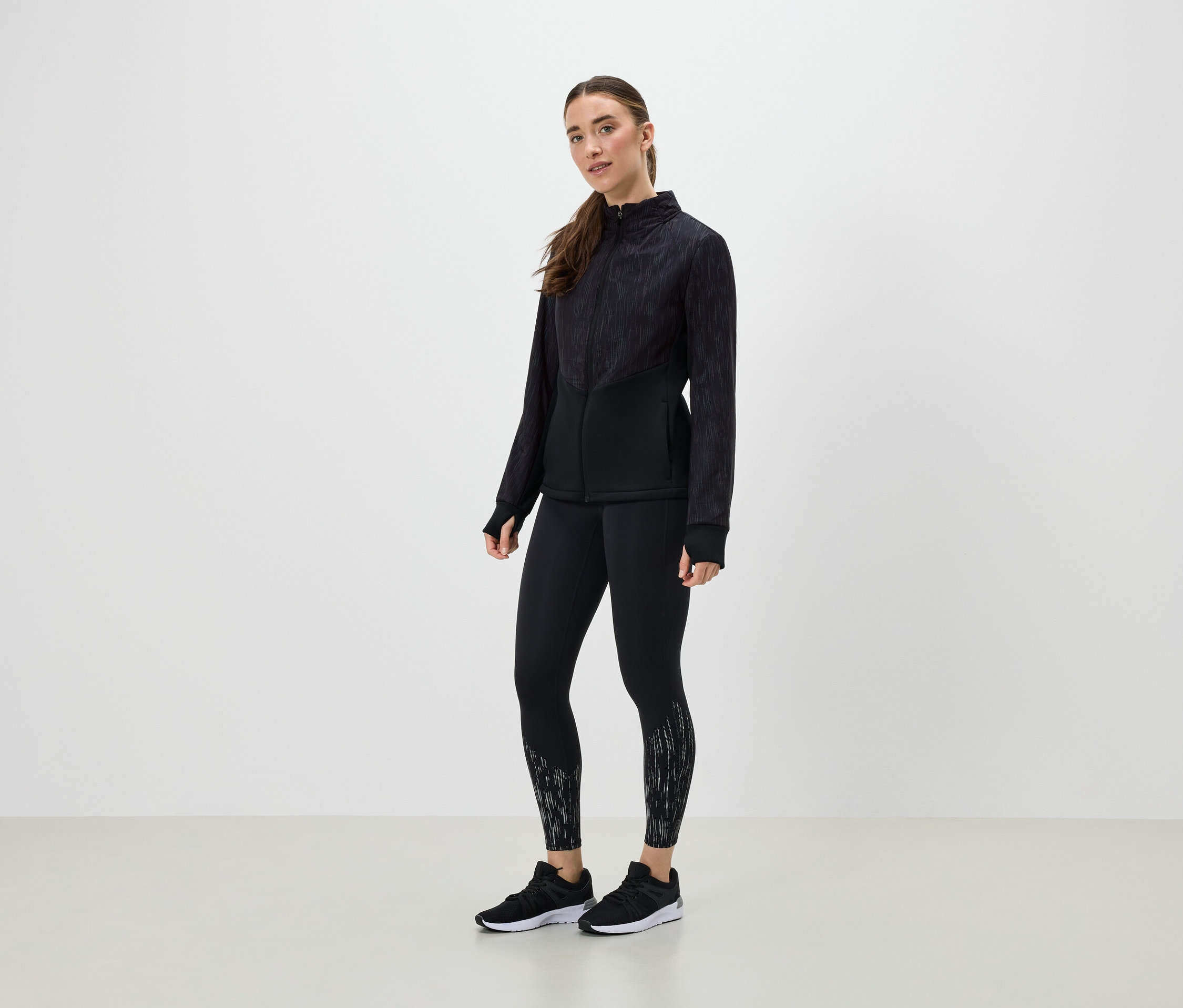 Eine Frau in schwarzer Sportbekleidung posiert vor einem hellen Hintergrund.