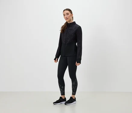 Eine Frau in schwarzer Sportbekleidung posiert vor einem hellen Hintergrund.
