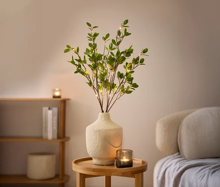 Zwei LED-Dekozweige in einer weißen Vase auf einem Holztisch.