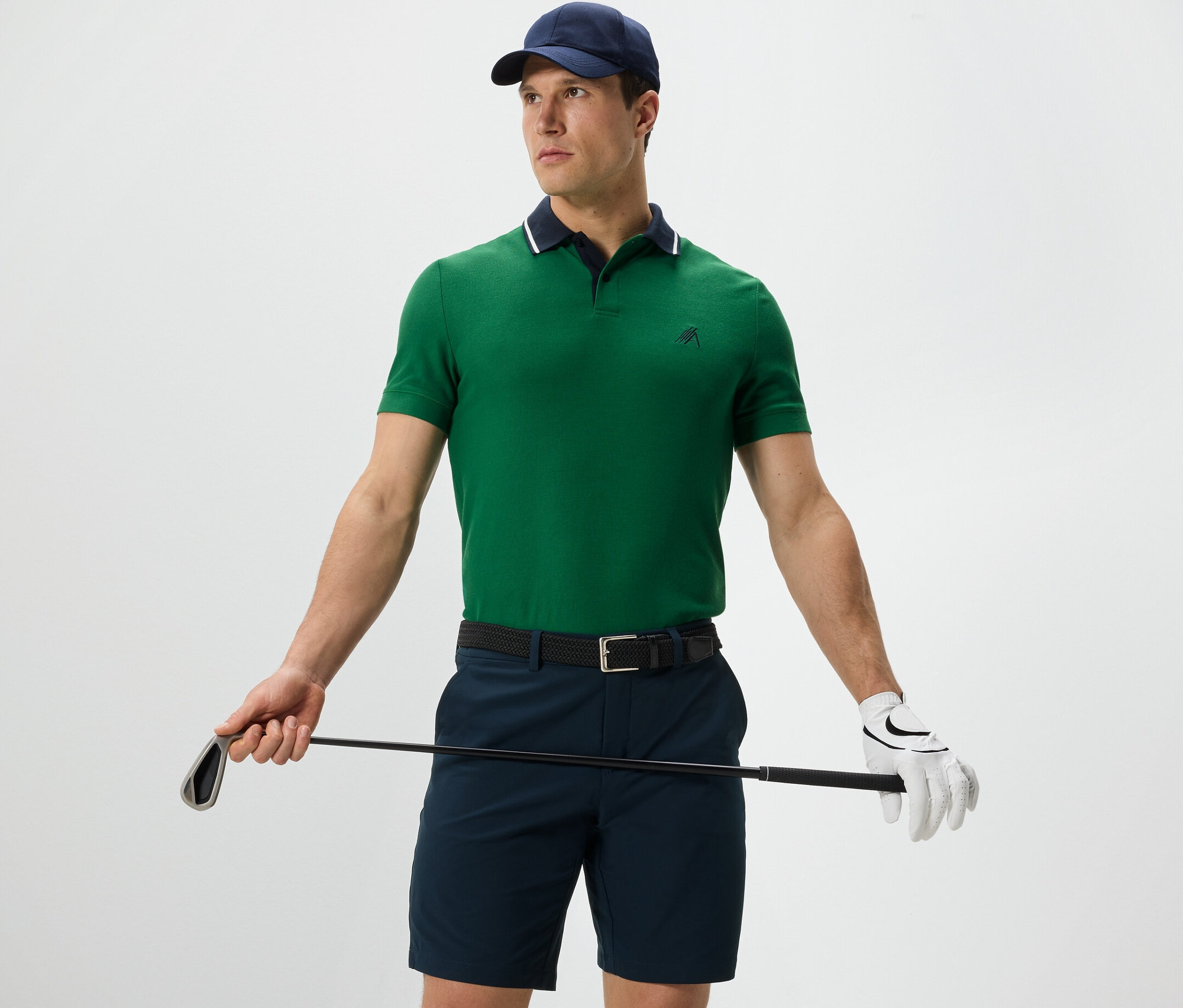 Mann hält Golfschläger und trägt ein grünes Funktions-Poloshirt.