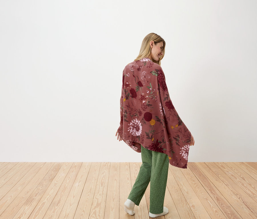 Frau blickt über die Schulter und posiert in einem geblümten Überwurf und grüner Hose.