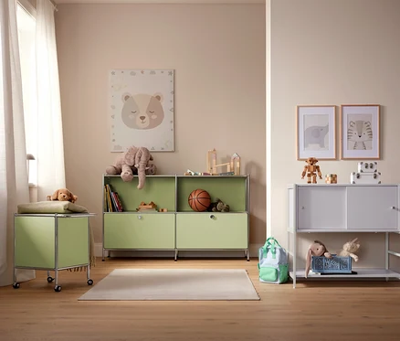 Ein Kinderzimmer mit hellgrünen und weißen Aufbewahrungsschränken, Spielzeug und Bildern an der Wand.