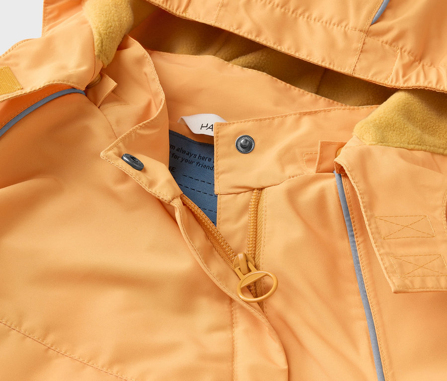 Nahaufnahme einer orangefarbenen Jacke mit Kapuze, gelbem Fleecefutter, Reißverschluss und Druckknöpfen.