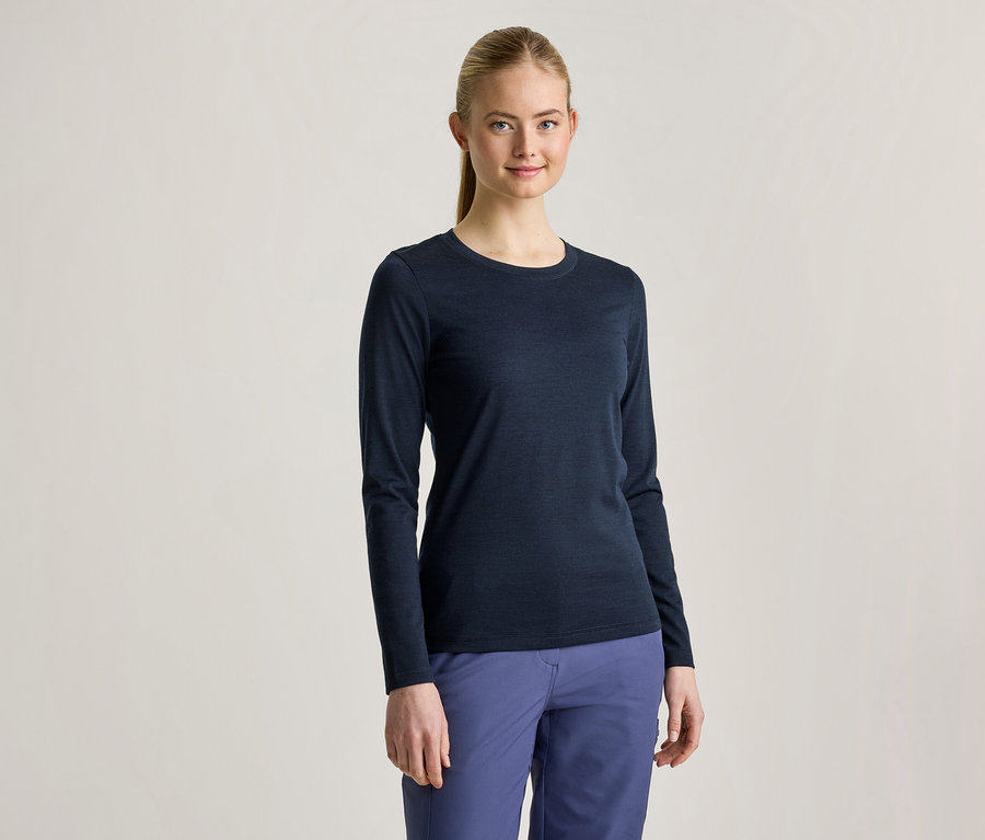 Eine junge Frau mit blondem Pferdeschwanz trägt ein dunkelblaues Langarmshirt und blaue Hosen, sie lächelt in die Kamera.