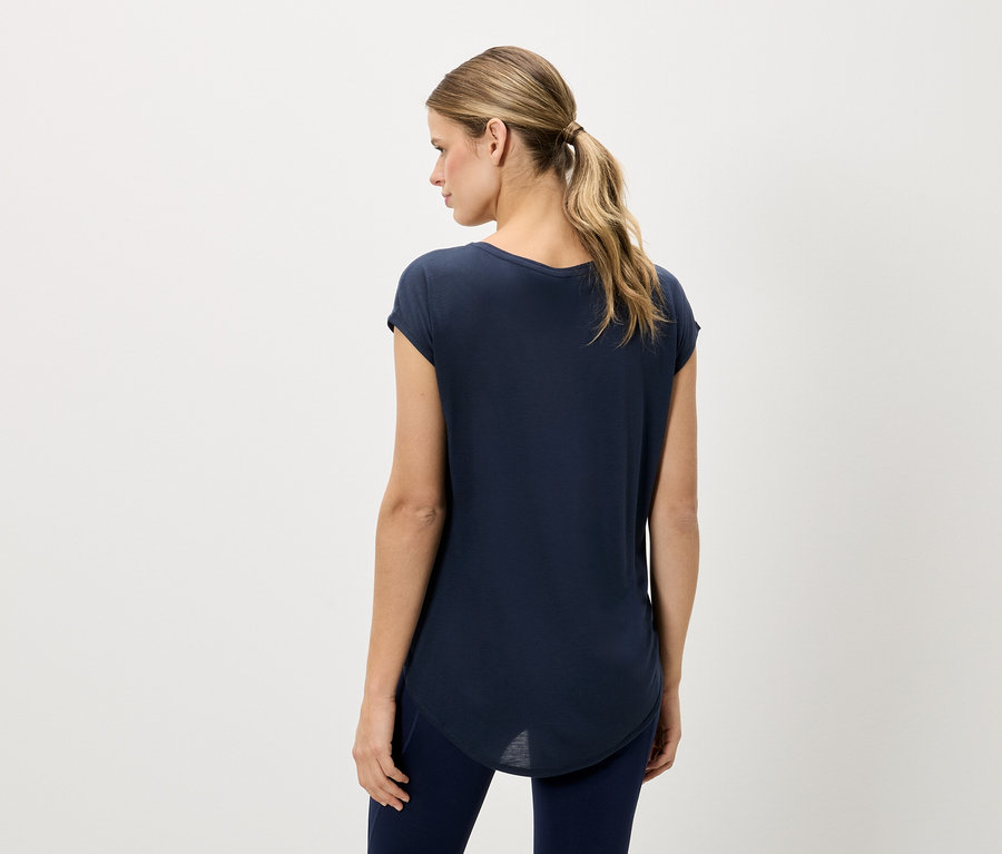 Frau von hinten, trägt ein marineblaues T-Shirt und marineblaue Leggings vor einem neutralen Hintergrund.
