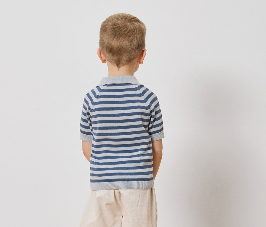 Rückansicht eines Kindes mit blonden Haaren, das ein blau-weiß gestreiftes Poloshirt und beigefarbene Shorts vor einem weißen Hintergrund trägt.