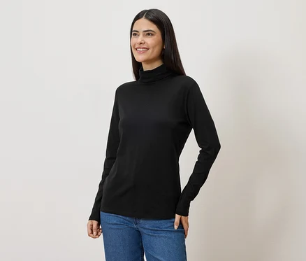 Eine Frau mit langen, dunklen Haaren trägt ein schwarzes Rollkragenshirt und Jeans.