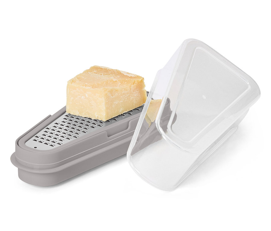Ein Stück Käse liegt auf einer grauen Reibe mit Behälter und transparentem Deckel.