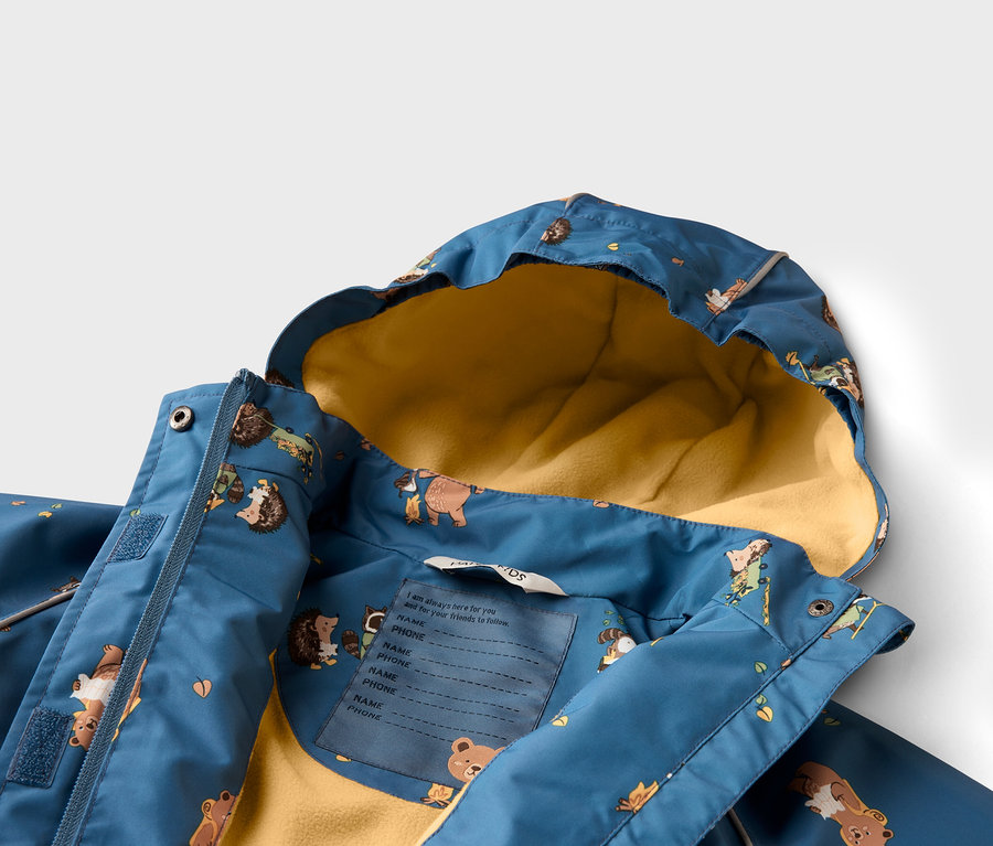 Nahaufnahme einer blauen Kinderjacke mit gelbem Innenfutter und Tiermuster. Ein Etikett für Name und Telefonnummer ist sichtbar.