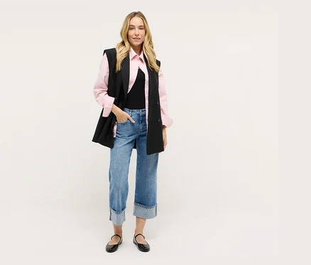Frau mit schwarzer Weste, rosa Hemd, Jeans und schwarzen Schuhen.