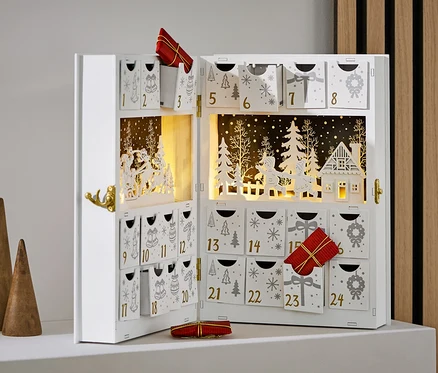 Offener, weißer Adventskalender mit Verzierungen und Geschenken, neben drei Holzkegeln.