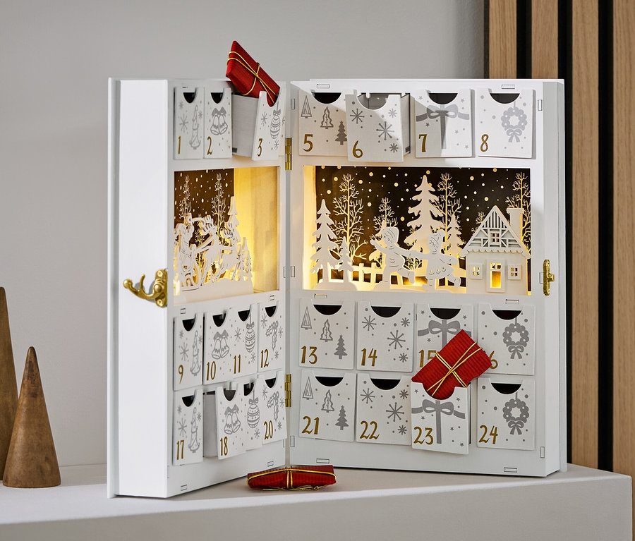 Offener, weißer Adventskalender mit Verzierungen und Geschenken, neben drei Holzkegeln.