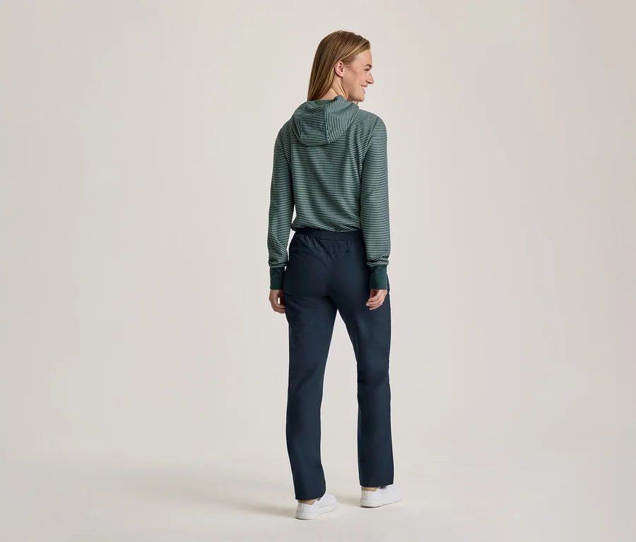 Person steht mit dem Rücken zur Kamera und blickt über die rechte Schulter. Sie trägt einen grün-weiß gestreiften Kapuzenpullover, dunkelblaue Hose und weiße Turnschuhe.