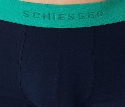 Nahaufnahme einer dunkelblauen Unterhose mit einem leuchtend grünen Bund, auf dem 'SCHIESSER' in dunkelgrünen Buchstaben zu sehen ist.