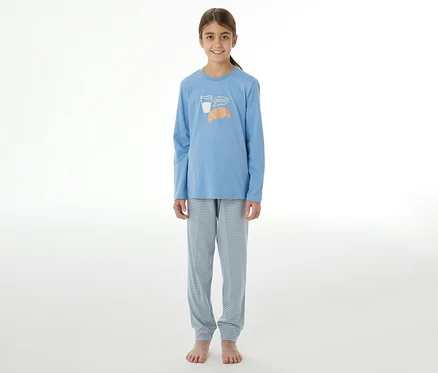 Junges Mädchen in einem blauen SCHIESSER Kinder-Pyjama mit Langarmshirt und gestreiften Hosen. Das Oberteil zeigt ein Glas Milch und ein Croissant mit „Bonjour“.