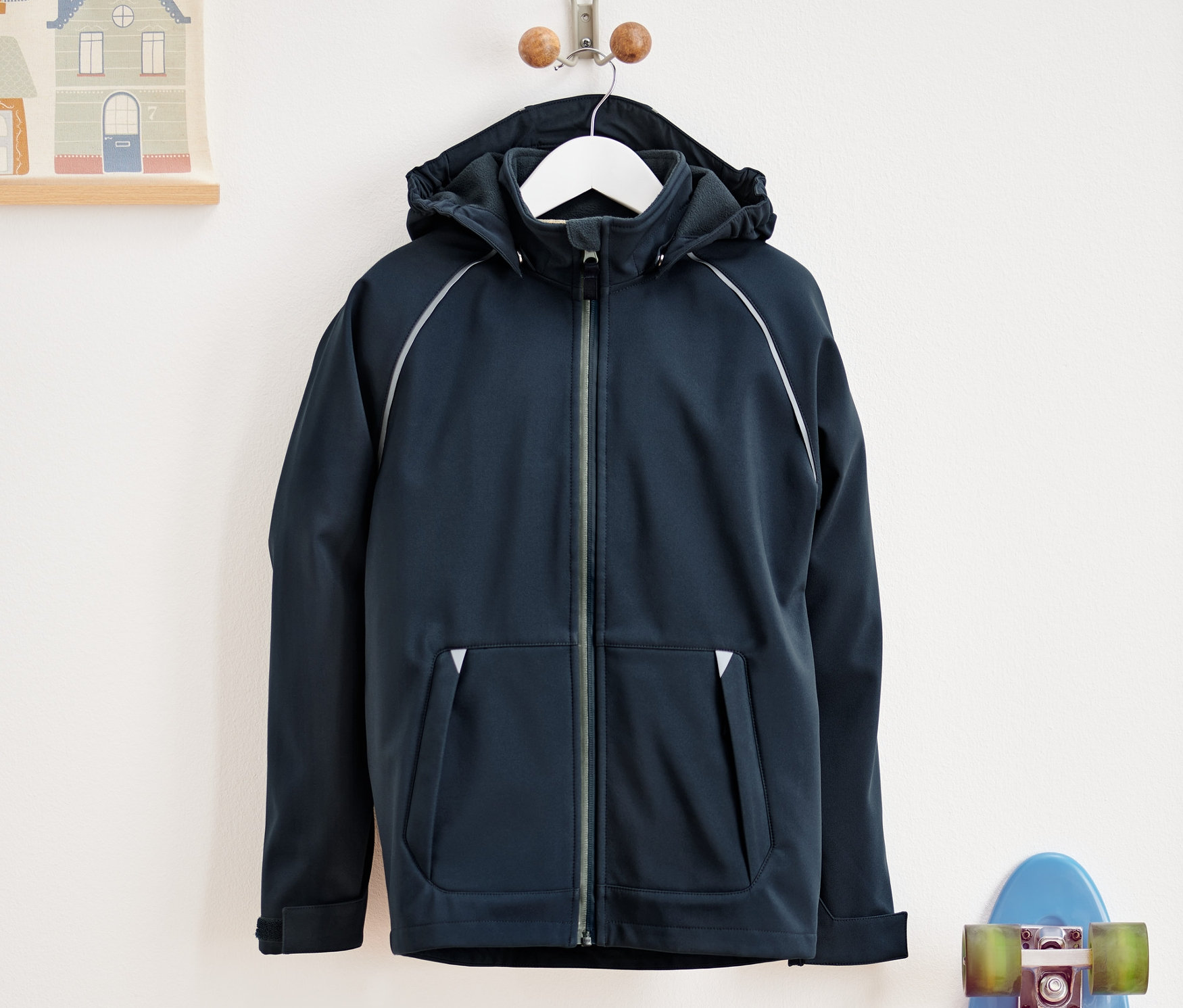 Eine marineblaue Softshell-Jacke hängt an einem Kleiderbügel neben einem blauen Skateboard.