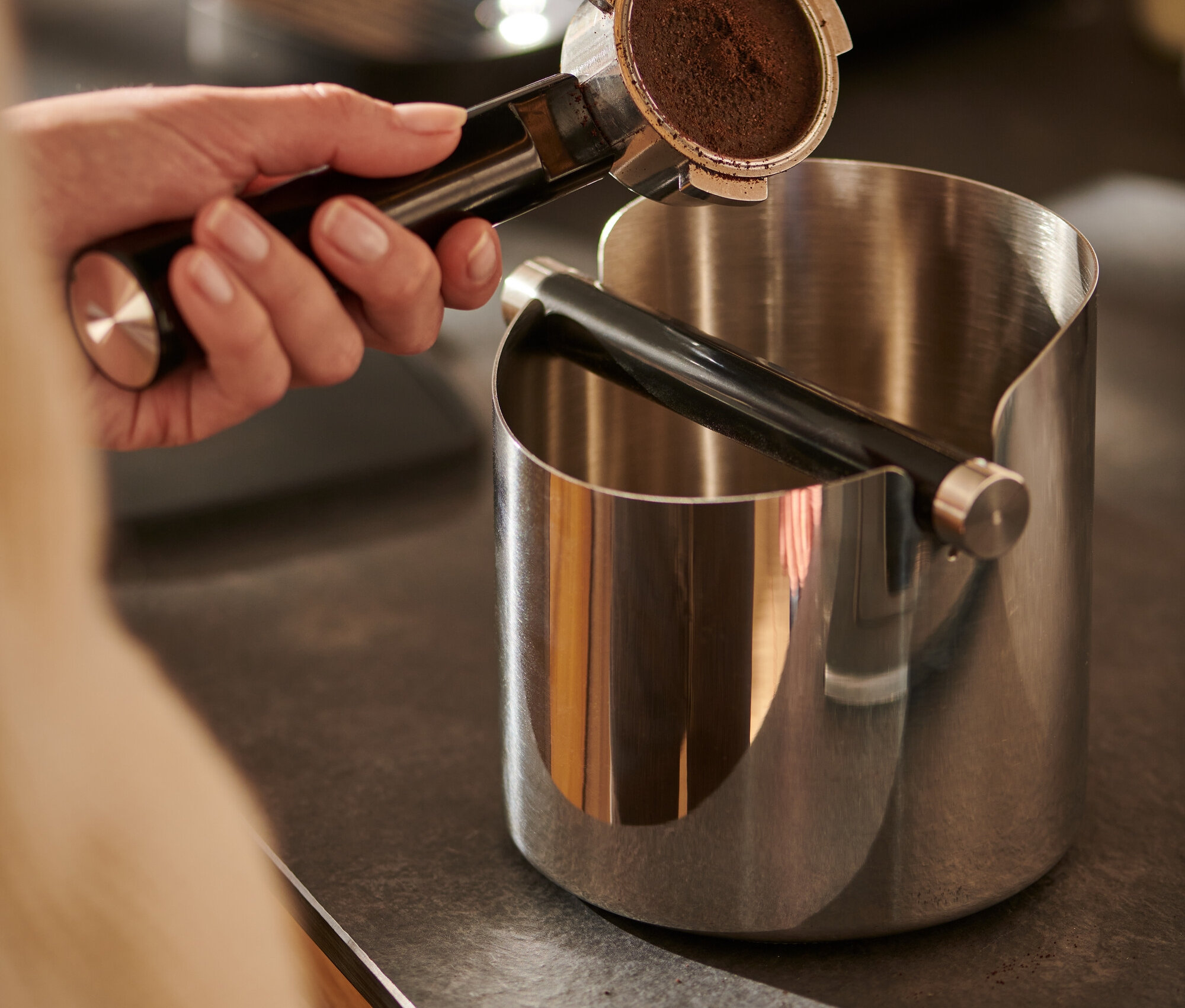 Hand hält Kaffeeträger über glänzender Knock Box.