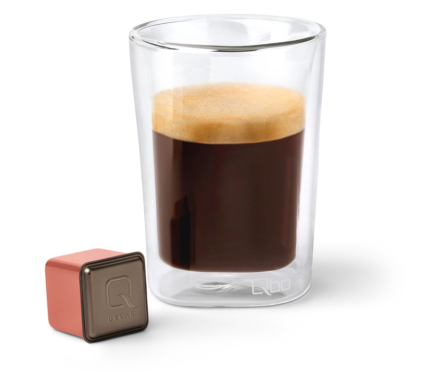 Eine Qbo Caffè MENOS CAFEÍNA Kapsel neben einem Glas Kaffee.