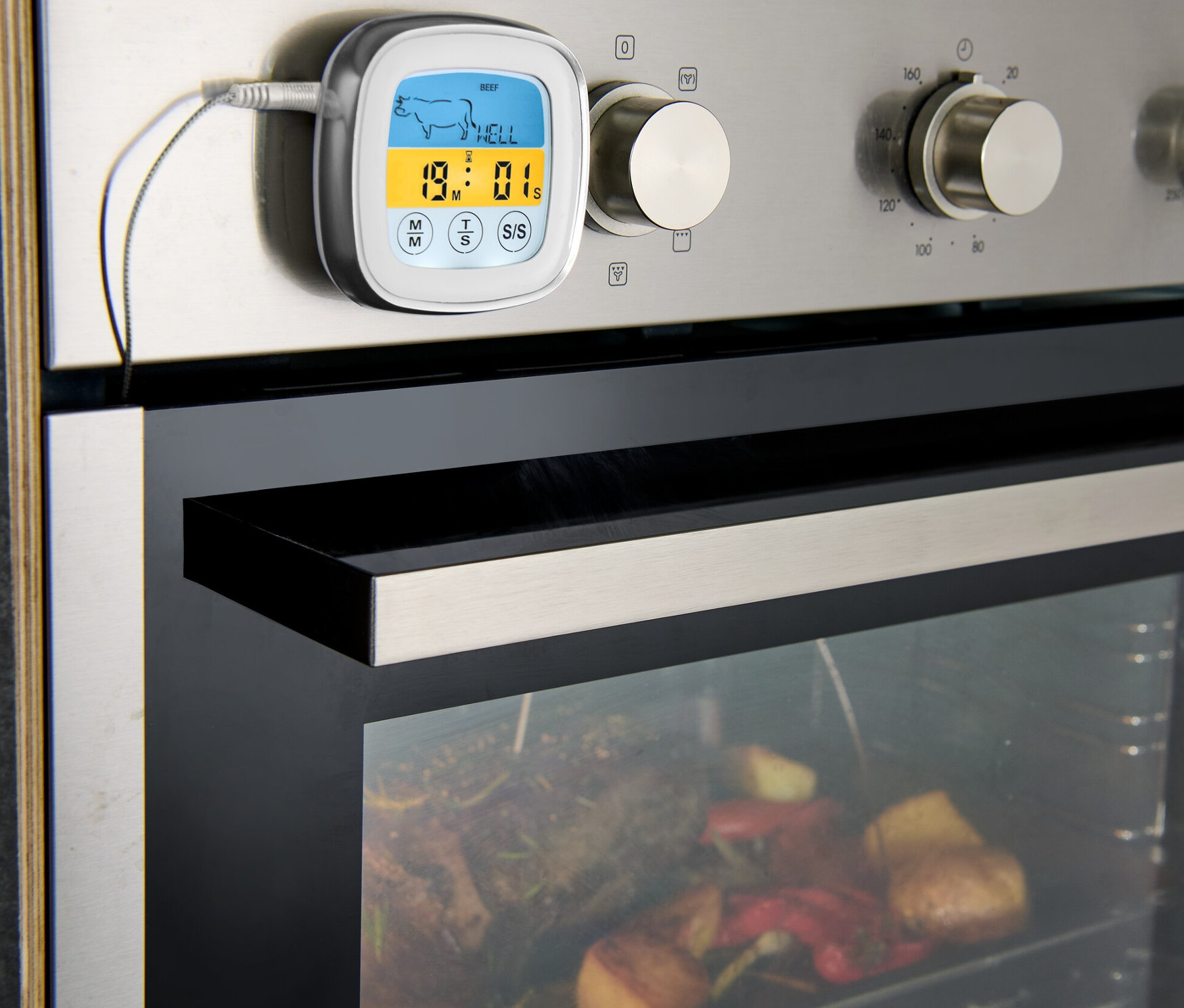 Ein Braten-Thermometer ist am Ofen befestigt, im Inneren befindet sich Braten mit Gemüse.