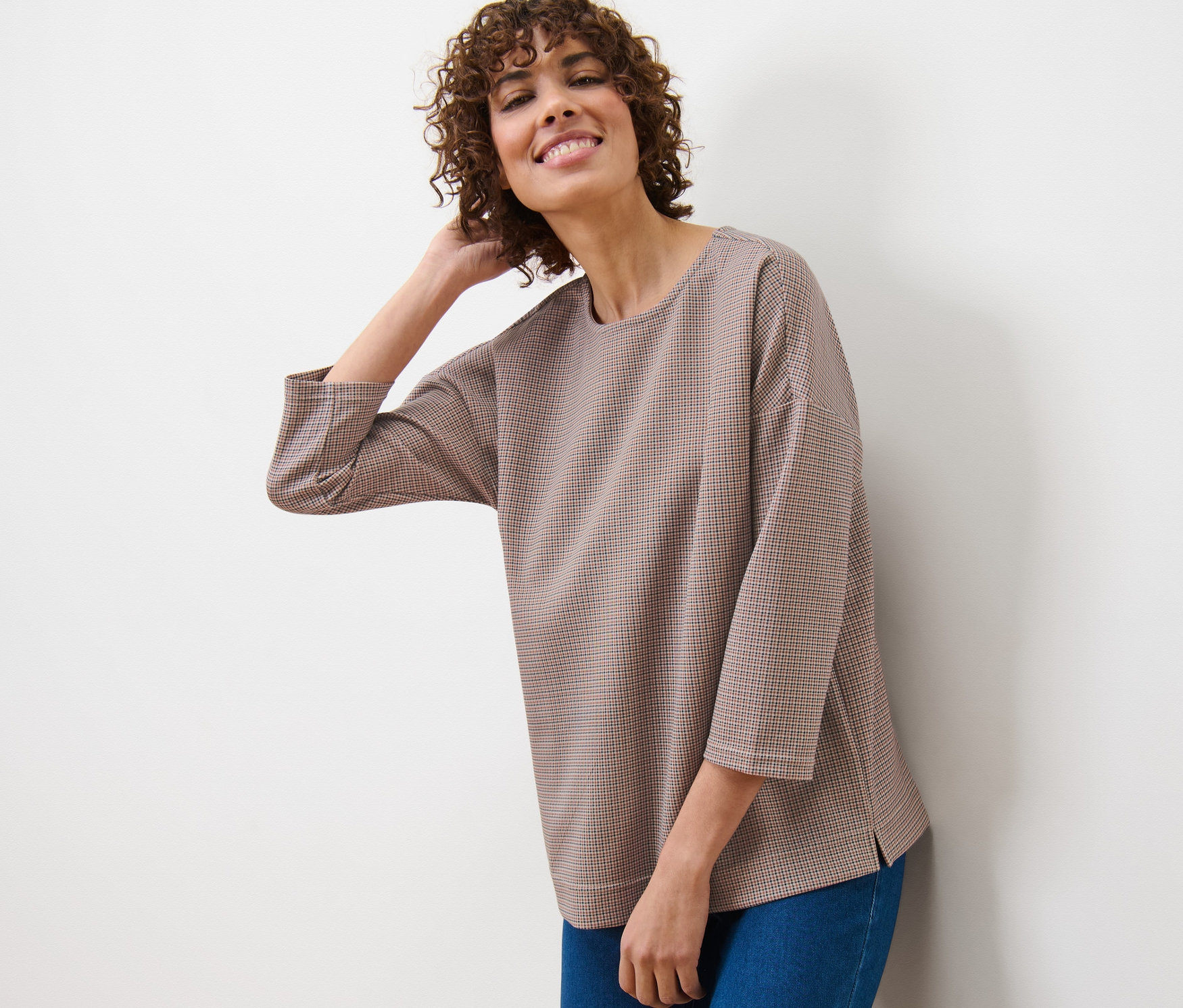 Frau lehnt an einer Wand und trägt ein kariertes Sweatshirt und Jeans.