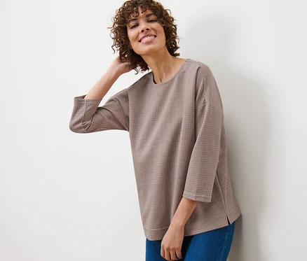 Frau lehnt an einer Wand und trägt ein kariertes Sweatshirt und Jeans.
