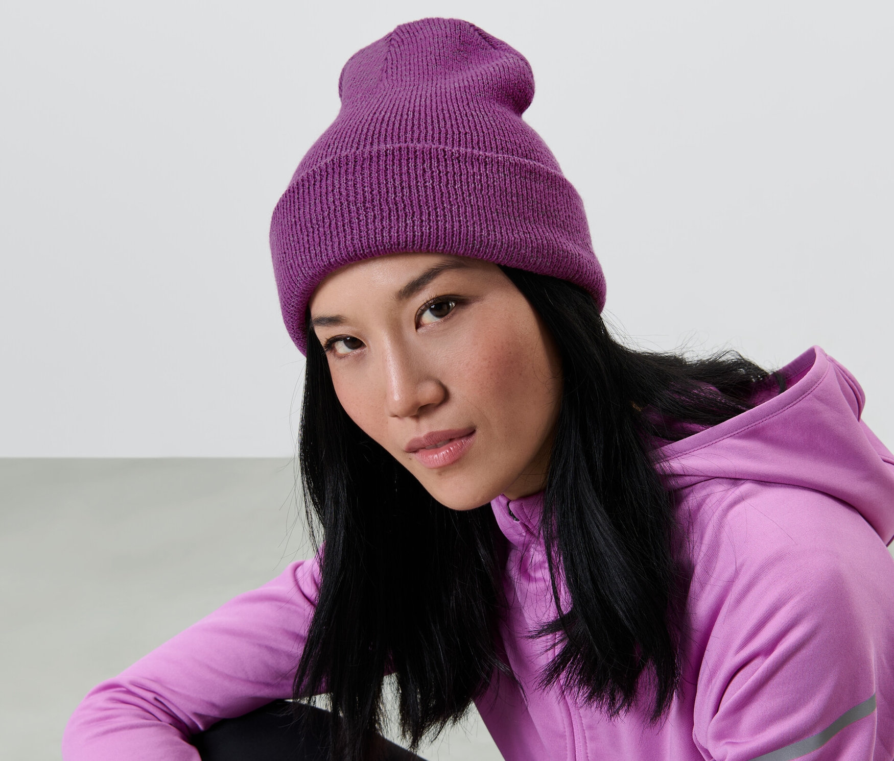 Asiatische Frau mit langen schwarzen Haaren trägt eine lila Strickmütze und einen lila Kapuzenpullover.