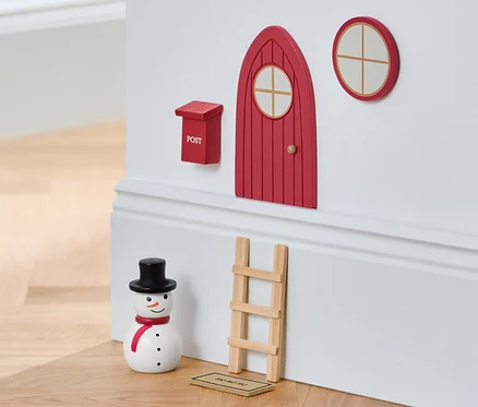 Ein Wichteltür-Set an einer Wand mit einem Schneemann und einem Hocker.