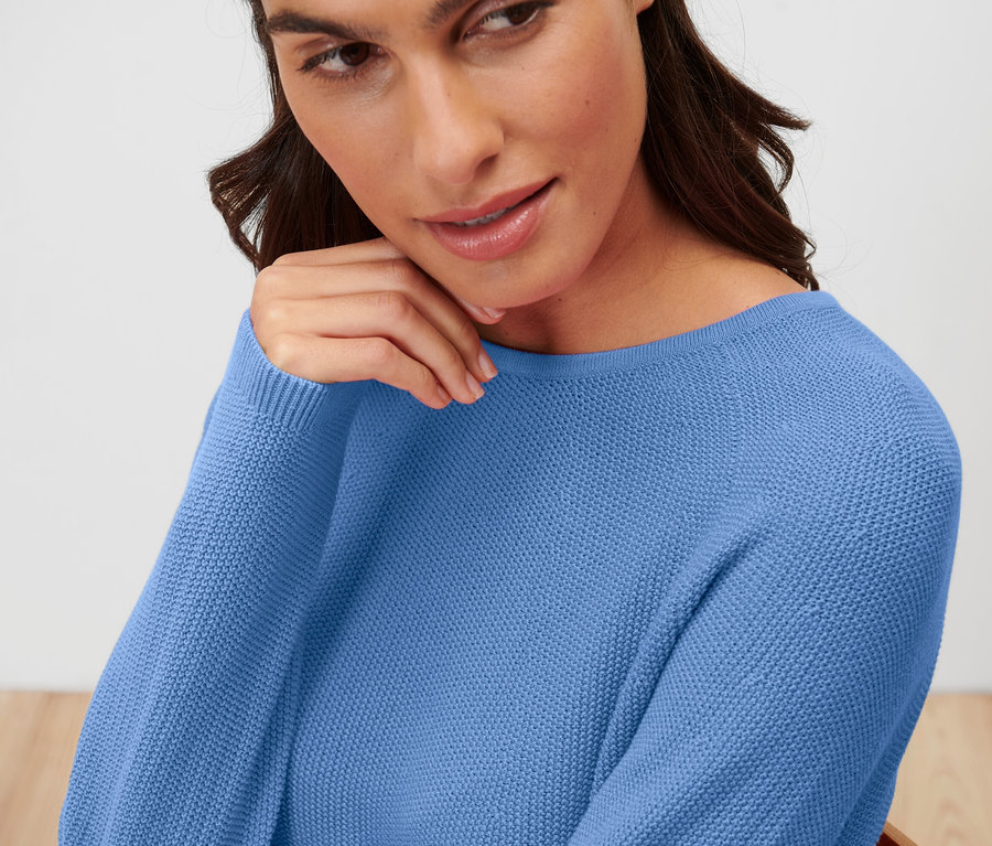 Frau mit braunen Haaren trägt einen blauen Strickpullover.