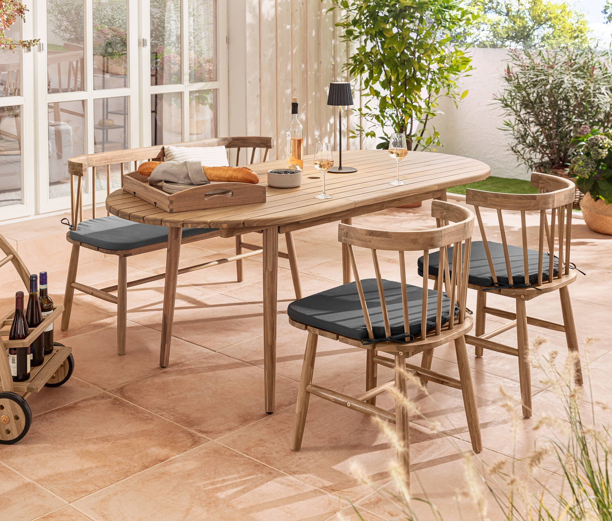 Outdoor-Szene mit ovalem Ausziehtisch, Dining-Stühlen mit Sitzpolster, Bank mit Sitzpolster, Barwagen und schwarzer LED-Akku-Outdoor-Tischleuchte.