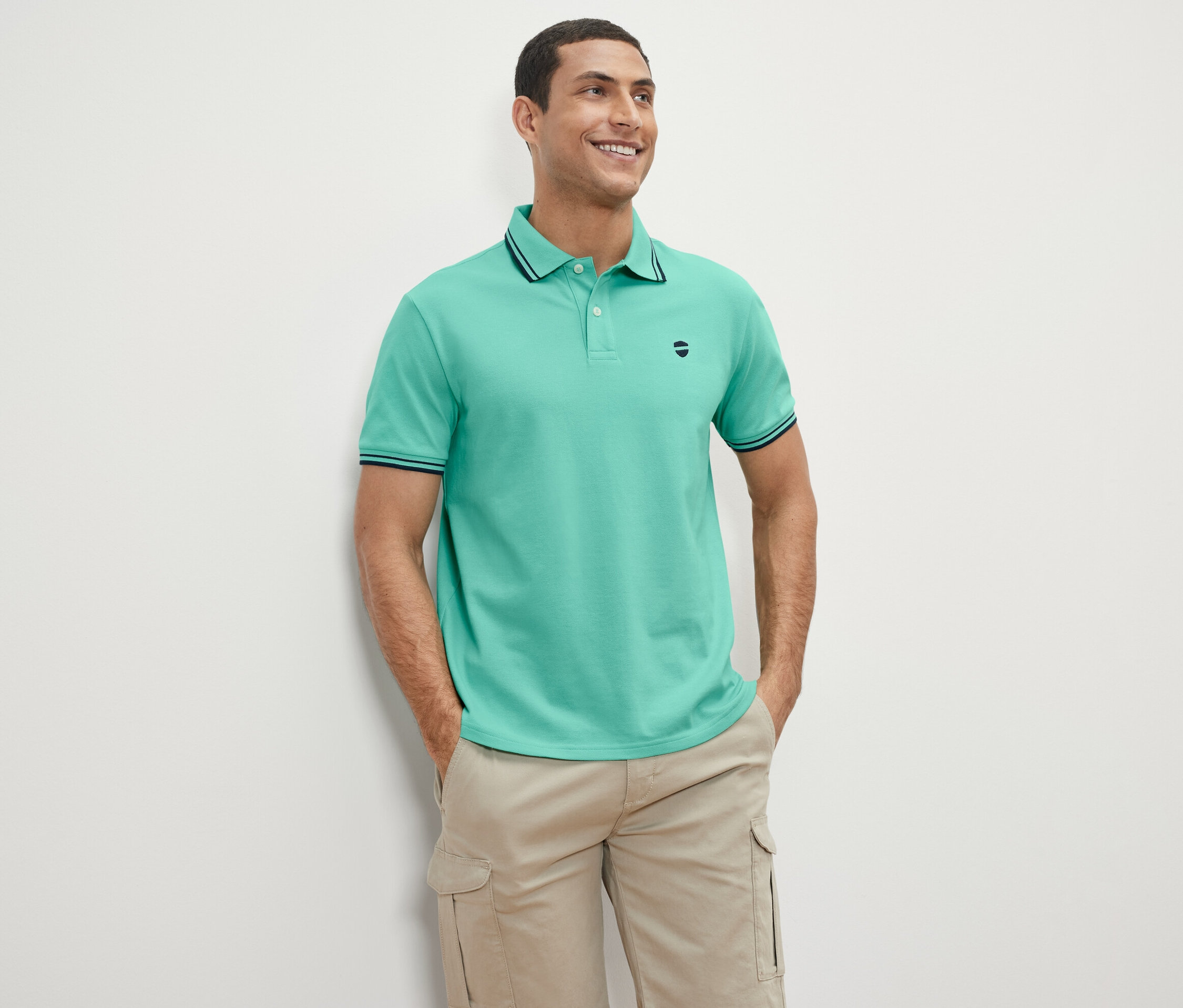 Ein Mann steht und lächelt, er trägt ein grünes Piqué-Poloshirt.