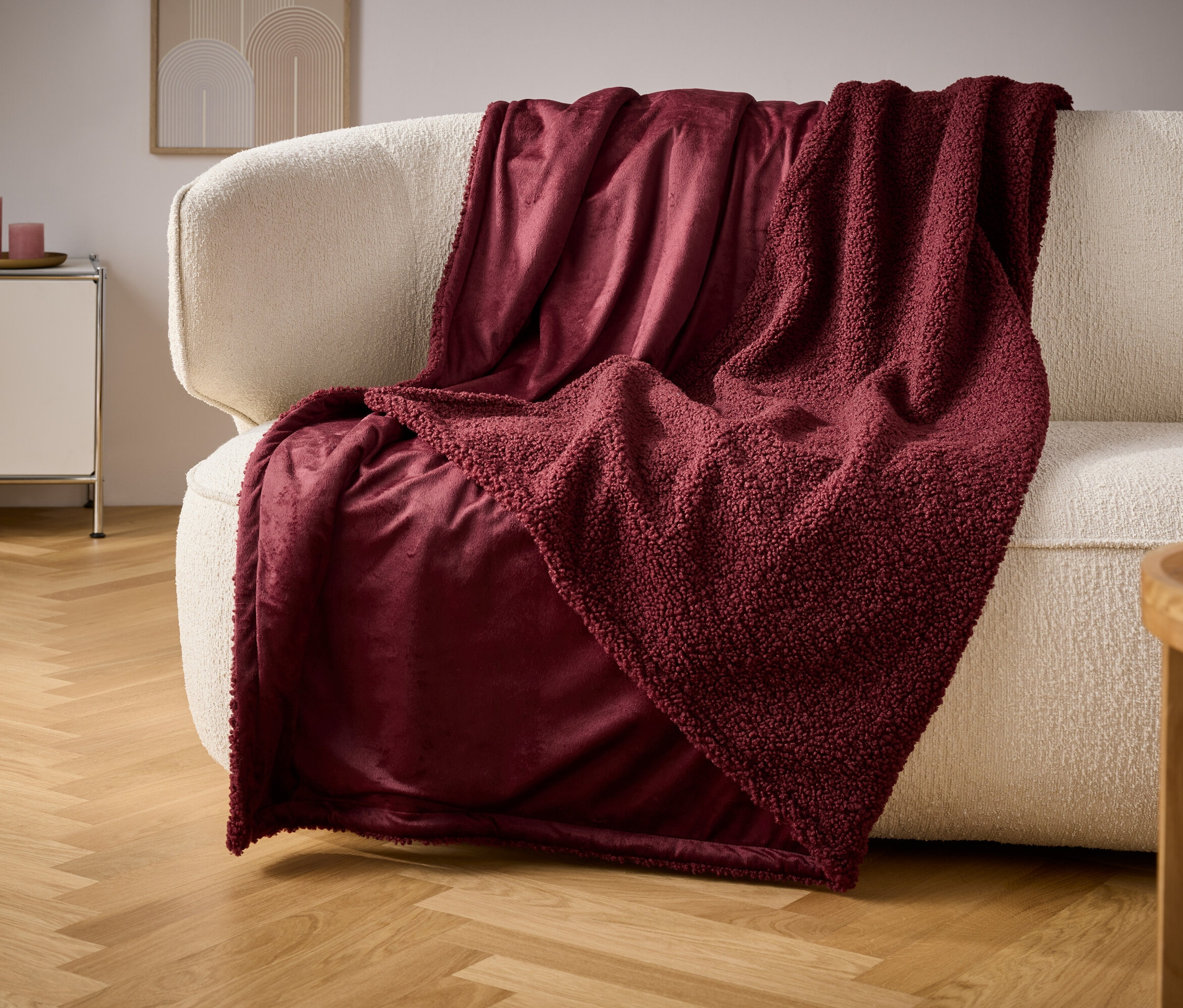 Eine weinrote Decke liegt auf einem cremefarbenen Sofa.