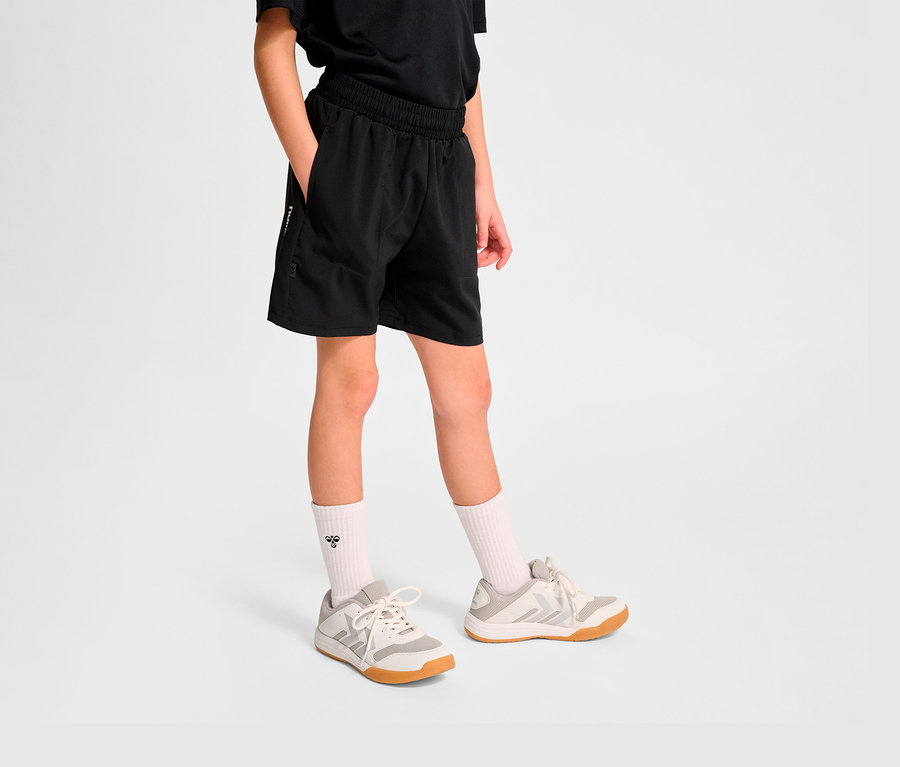 Junge trägt schwarze HUMMEL HMLJR Pulse Workout Shorts und Turnschuhe.