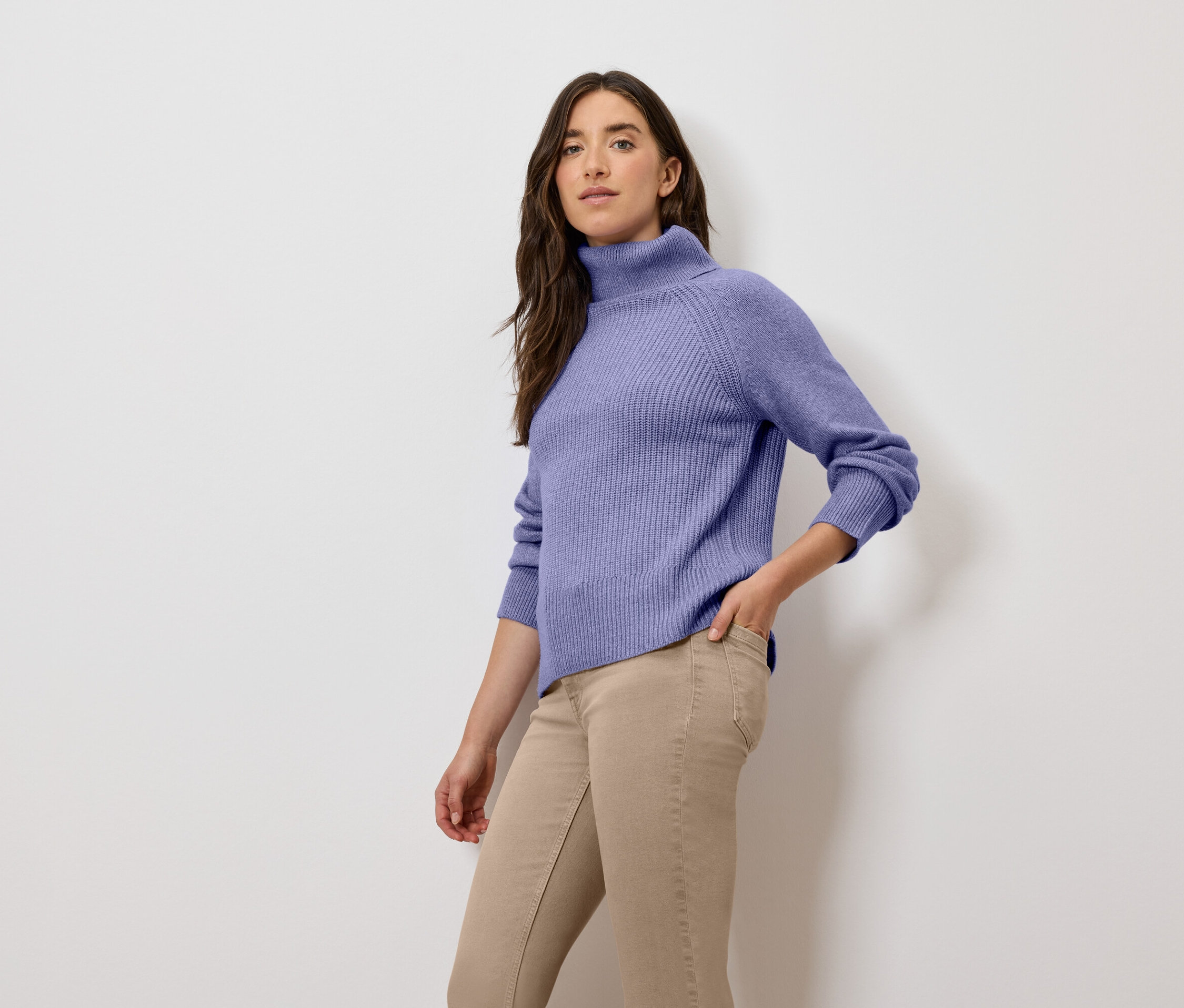 Frau posiert in lila Rollkragenpullover und beigen Hosen.