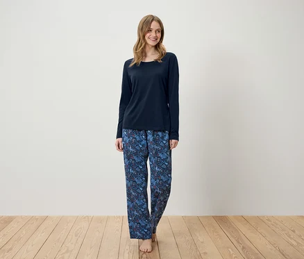 Eine Frau steht und trägt einen dunkelblauen Schlafanzug mit langen Ärmeln und eine blaue Hose mit Muster.