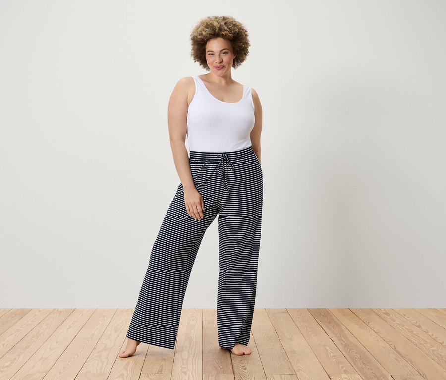 Frau posiert in weißem Tanktop und gestreiften Hosen.