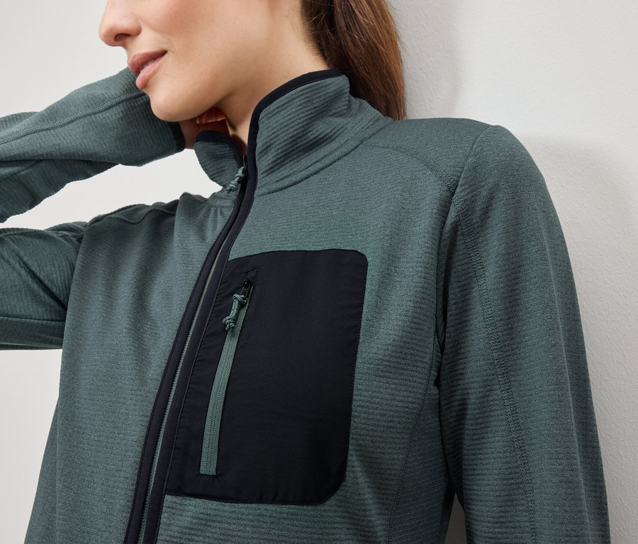 Detailaufnahme einer petrolfarbenen Damen-Fleecejacke mit langen Ärmeln und einer schwarzen Reißverschlusstasche auf der Brust.