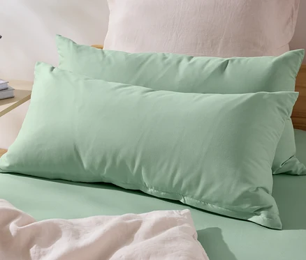 Zwei grüne Microfaser-Kopfkissenbezüge (ca. 80 x 40 cm) liegen auf einem Bett. Auf dem Nachttisch stehen eine Vase mit Blumen und Bücher.