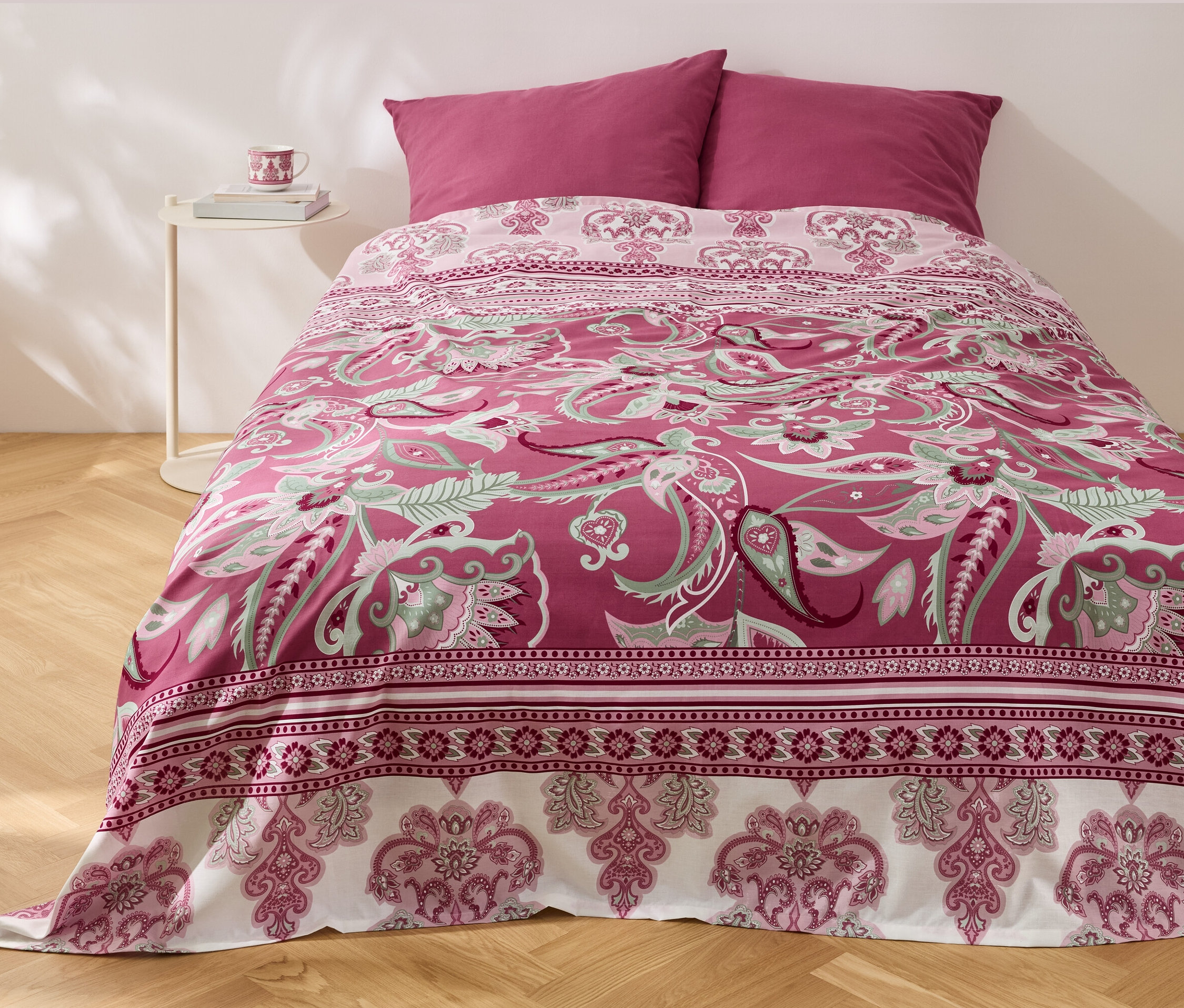 Ein Bett mit einem Renforcé-Multifunktions-Überwurf mit Blumenmuster und zwei Kissen.