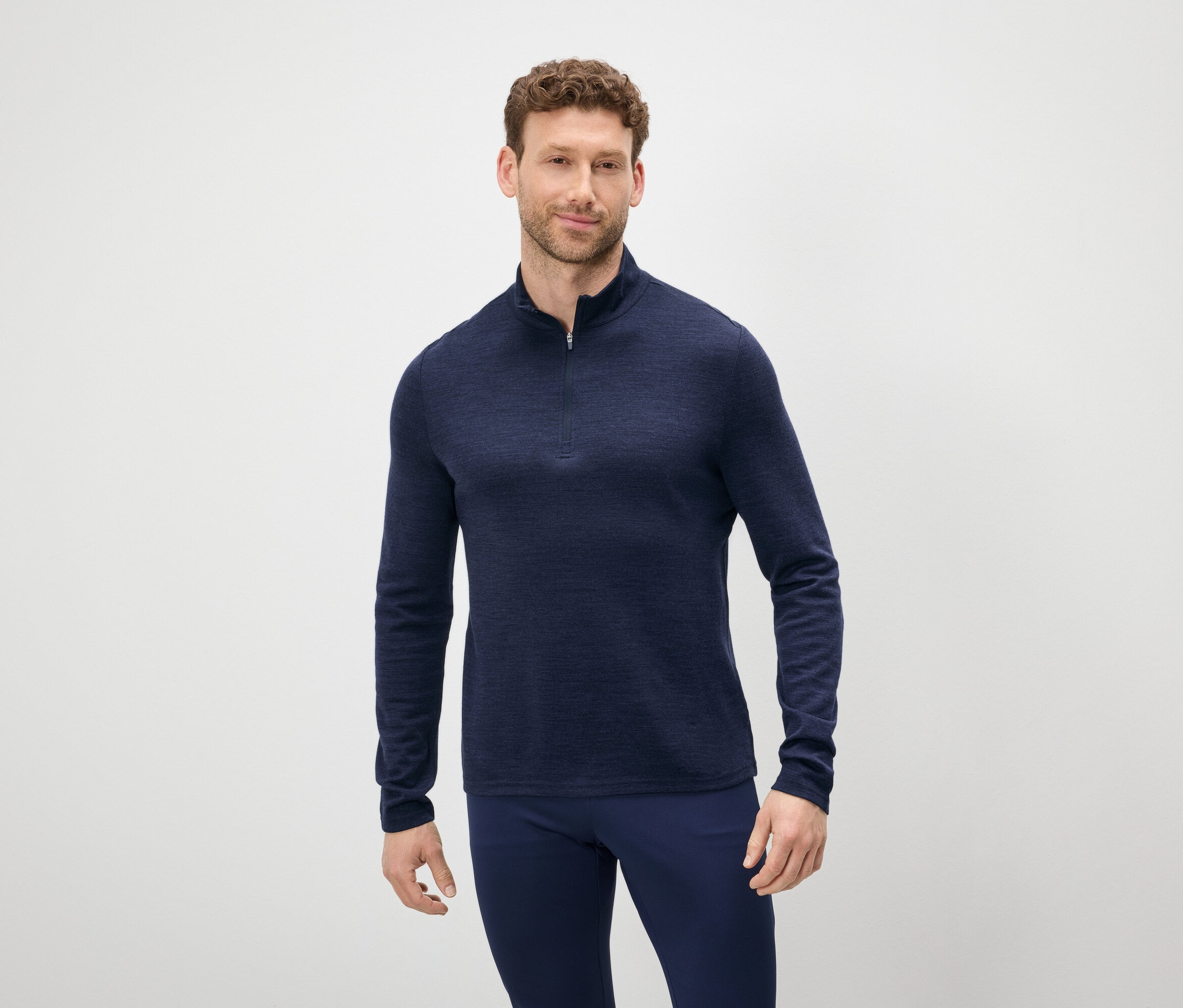 Mann mit braunen Haaren und Bart trägt einen blauen Pullover mit Reißverschluss und blaue Hosen.