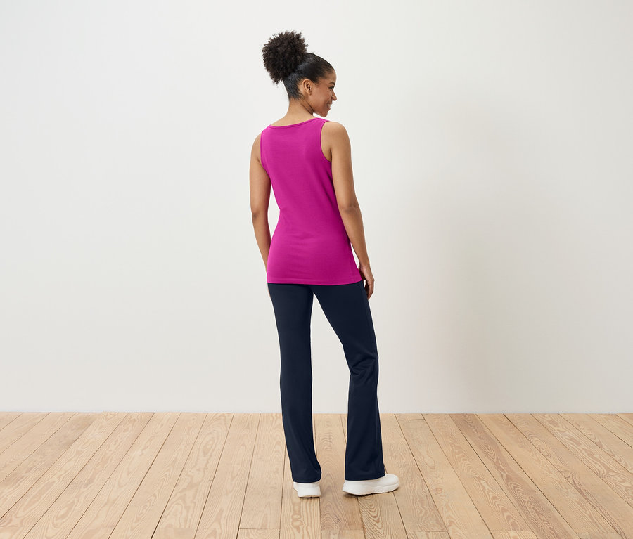 Frau steht mit dem Rücken zum Betrachter und trägt ein pinkes Top und dunkelblaue Hosen.