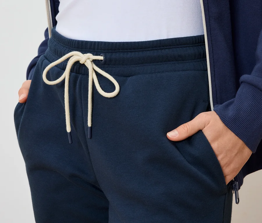Person mit Händen in den Taschen einer dunkelblauen Jogginghose mit hellem Kordelzug.